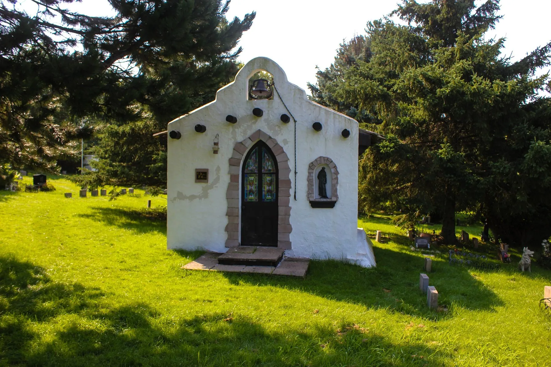 A small white chapel on the lawn of a pet cemetery, surrounded by trees